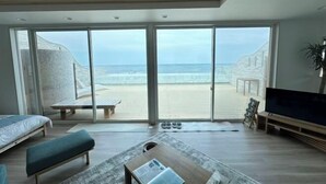 Quarto moderno com uma grande porta de vidro deslizante que dá para a praia, uma cama, um banco, uma mesa de centro e uma televisão.