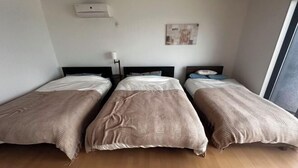 A room with three single beds, a wall-mounted air conditioner, a floor lamp, and a painting. - Lapita Resort (Sakai)