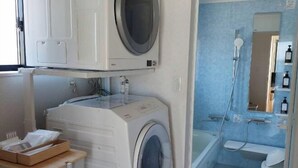 A compact laundry room with a washing machine, dryer, and a small table with a basket. - Lapita Resort (Sakai)