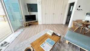 Uma sala de estar moderna com televisão, piso de madeira, sofá, mesa de centro e uma porta deslizante para uma varanda.