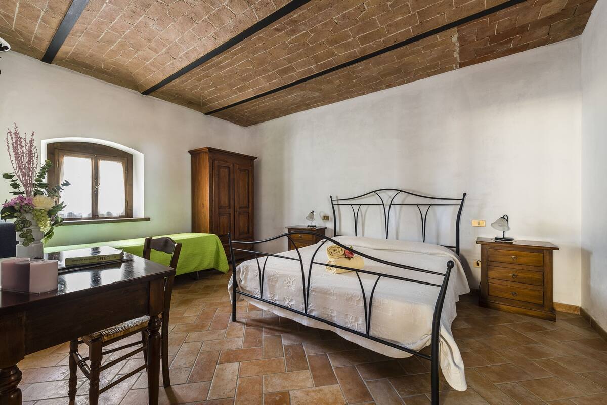 Een slaapkamer met een bed, een bureau, een stoel, een raam en een houten kast.
