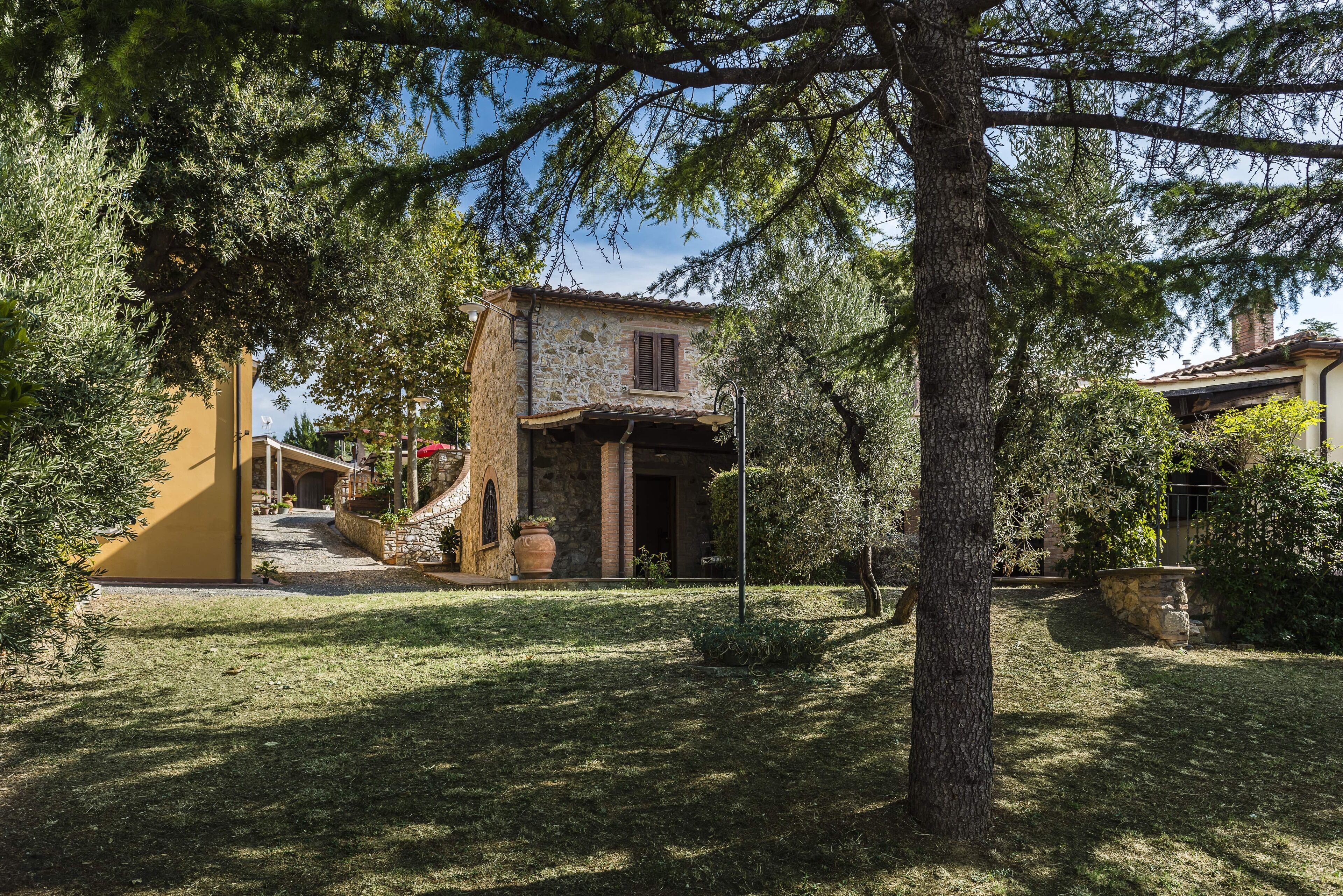 A stone building with a tiled roof, surrounded by trees and a well-maintained lawn.