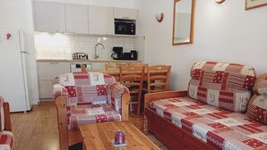 A compact living space with a kitchenette, a wooden dining table, a patterned sofa, and matching armchairs.