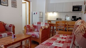 A cozy living room with a wooden sofa and chairs, a wooden coffee table, and a kitchen area with white cabinets and a microwave.