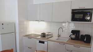 A compact kitchen with white cabinets, a microwave, a sink, a coffee maker, and a dishwasher.