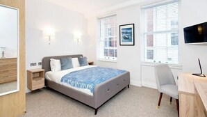 A bedroom with a bed, bedside tables, a chair, and a TV. - Eldon Chambers Pod 1 by City Living London (London)