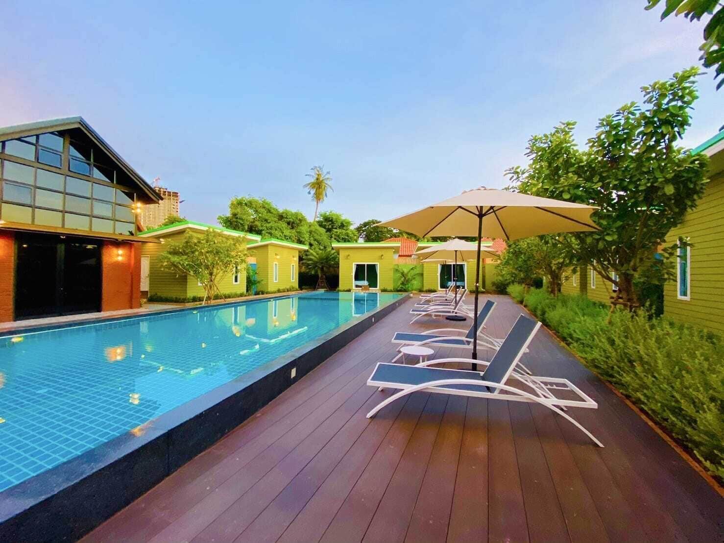 Ein Swimmingpool mit Liegestühlen und Sonnenschirmen, umgeben von Grünflächen und Gebäuden.