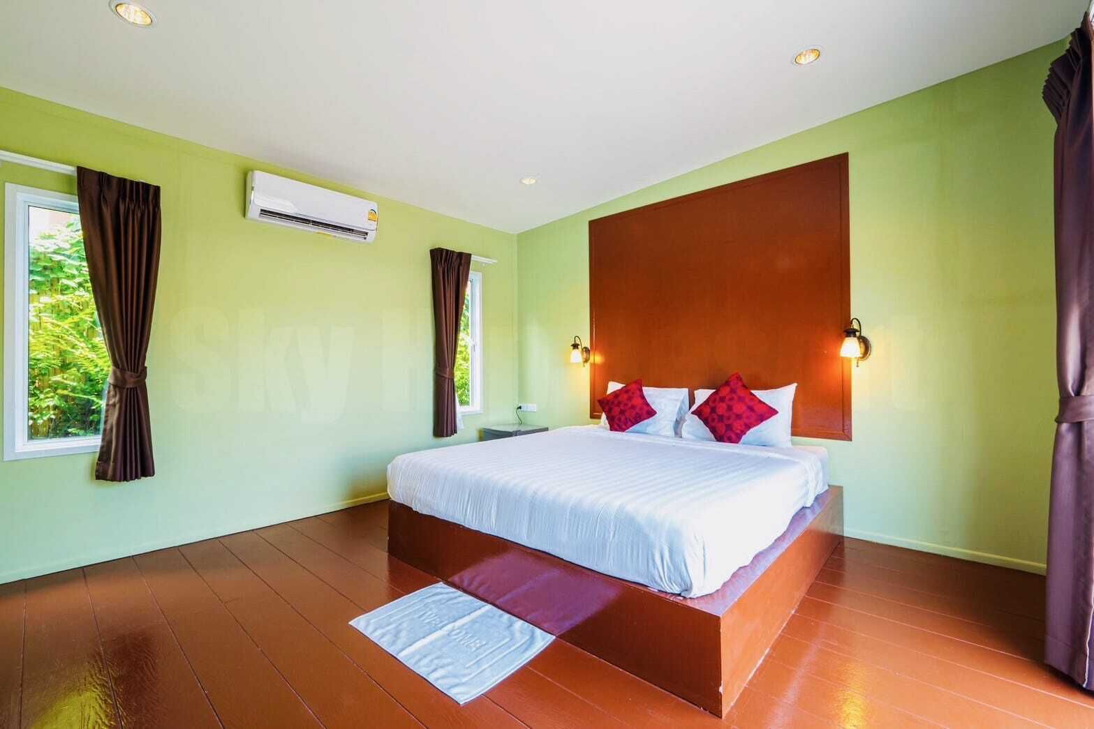 A bedroom with a large bed, green walls, wooden flooring, and an air conditioning unit.