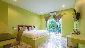 A hotel room with a bed, a desk, a chair, a TV, and a balcony with curtains.