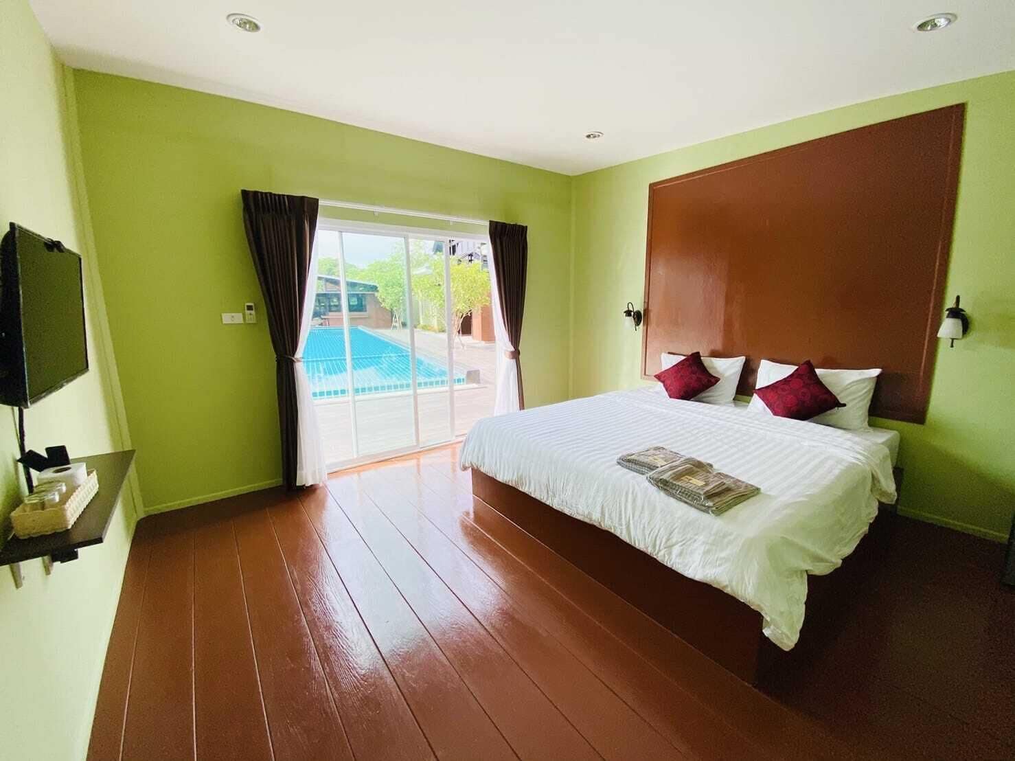 A hotel room with a large bed, a flat-screen TV, and a view of a swimming pool through a sliding door.