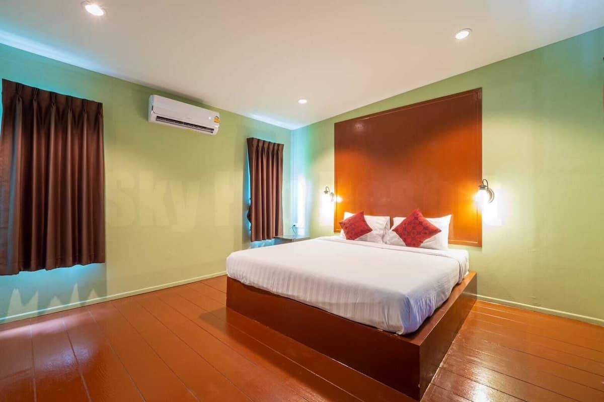 A hotel room with a large bed, an air conditioning unit, and a wooden floor.