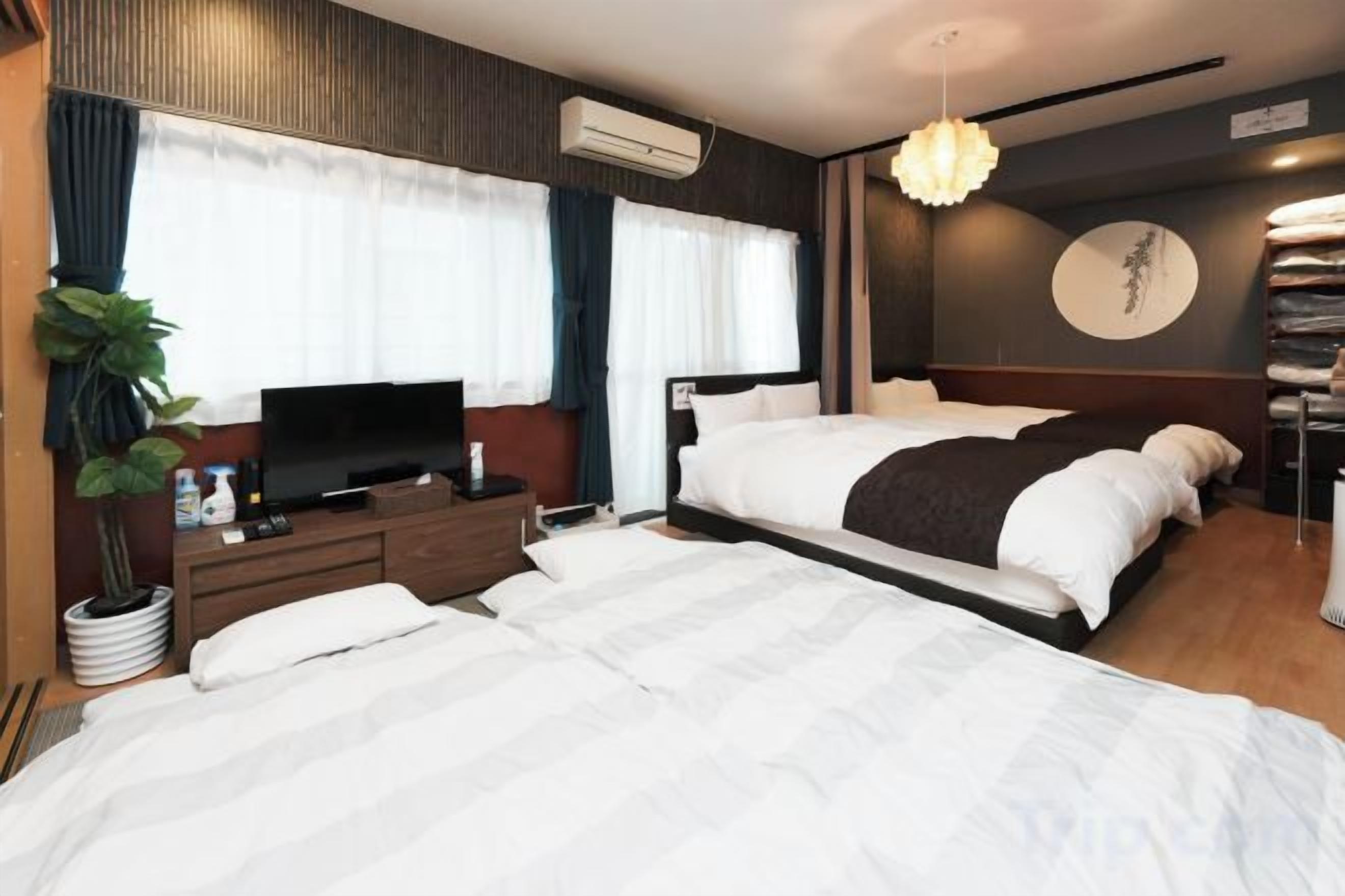 A hotel room with a large bed, a TV, a bedside table, and a potted plant.
