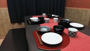 A dining table set with various bowls, plates, and chopsticks, with a red placemat and a black tablecloth. - Prosupa 5th #501 (Nagoya)