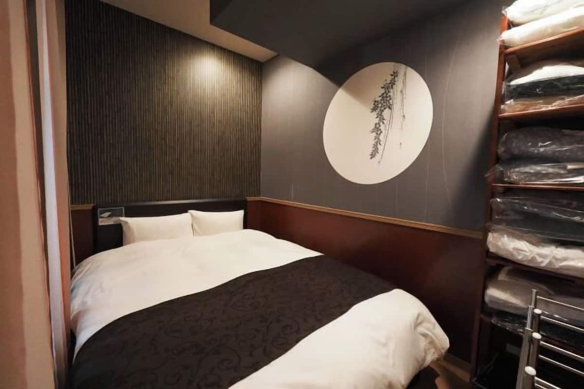 A hotel room with a bed, a wall-mounted circular artwork, and a shelving unit with folded linens.