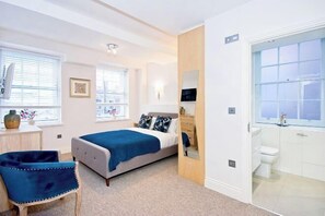 Een slaapkamer met een bed, een stoel, een dressoir en een badkamer met toilet en wastafel.