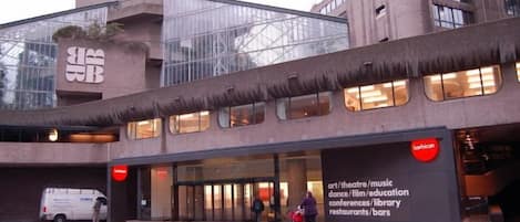 Un edificio moderno con entrada de vidrio y un cartel que indica que alberga un teatro de arte, música, cine, educación, congresos, biblioteca y restaurantes.