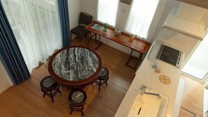 Ein Essbereich mit einem runden Tisch, vier Hockern, einer Holzbank und einem kleinen Tisch mit einer Vase und einem Buch.