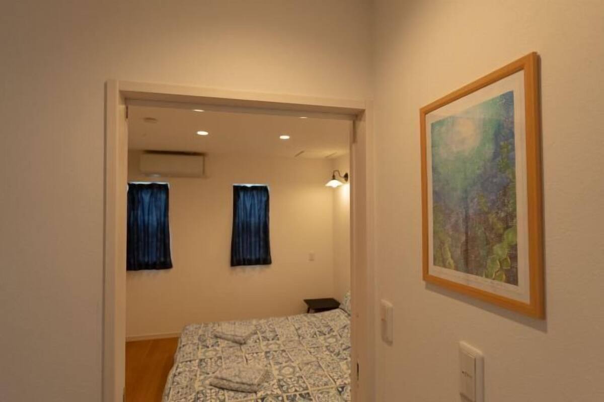 Quarto com cama, duas cortinas, um quadro e uma pequena mesa.