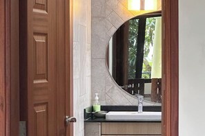 Een badkamer met een houten deur, een ronde spiegel, een wastafel en een groene zeepdispenser.
