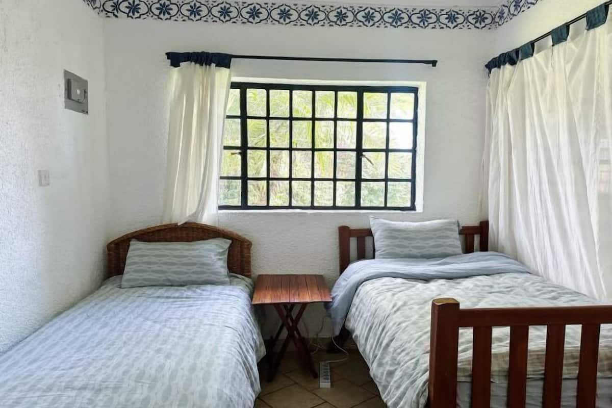 Un alojamiento pequeño y con una sola habitación, con dos camas individuales, una mesita y una ventana con vistas a zonas verdes.