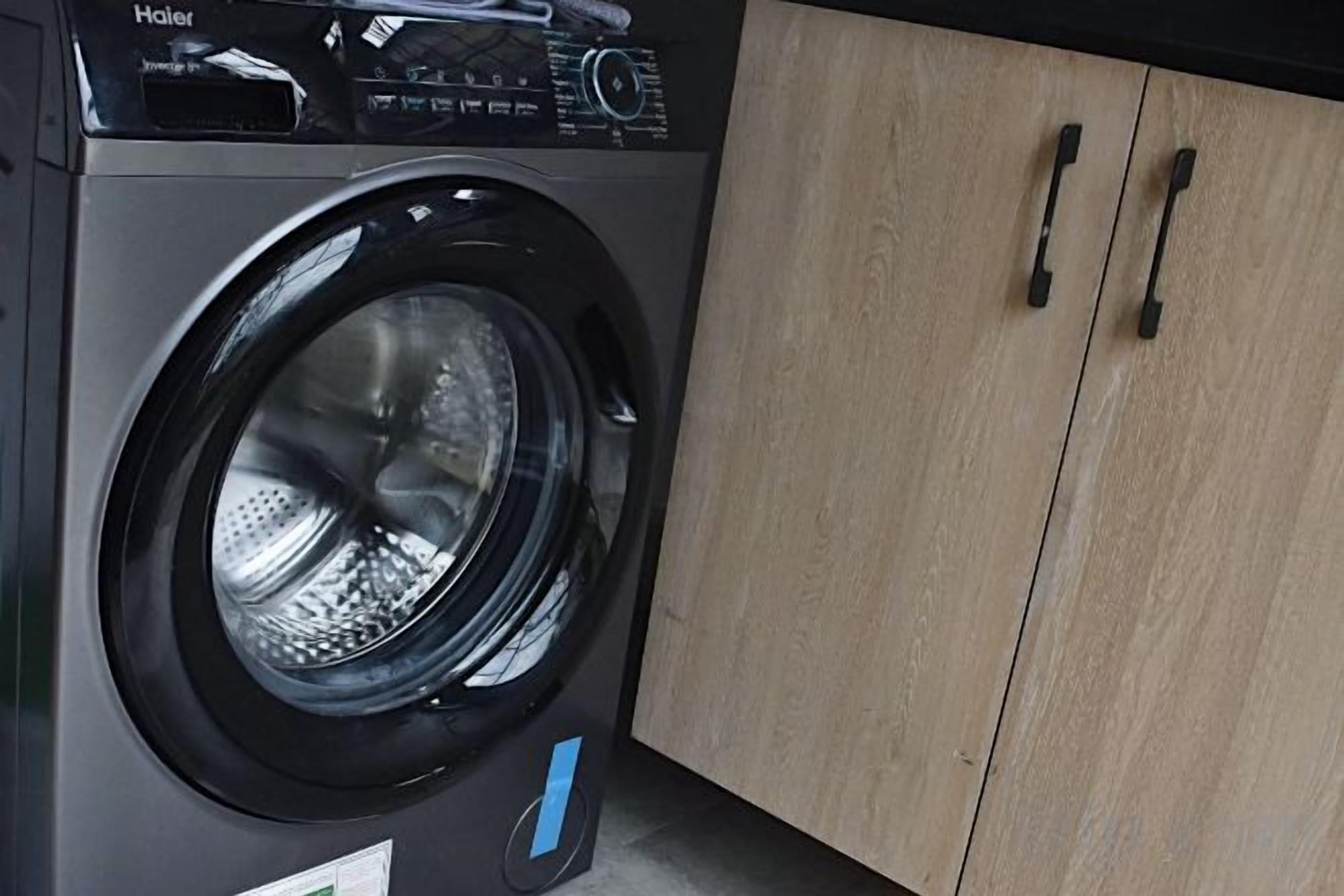 A front view of a modern washing machine with a control panel, located in a room with wooden cabinets.