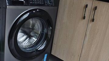 A front view of a modern washing machine with a control panel, located in a room with wooden cabinets.