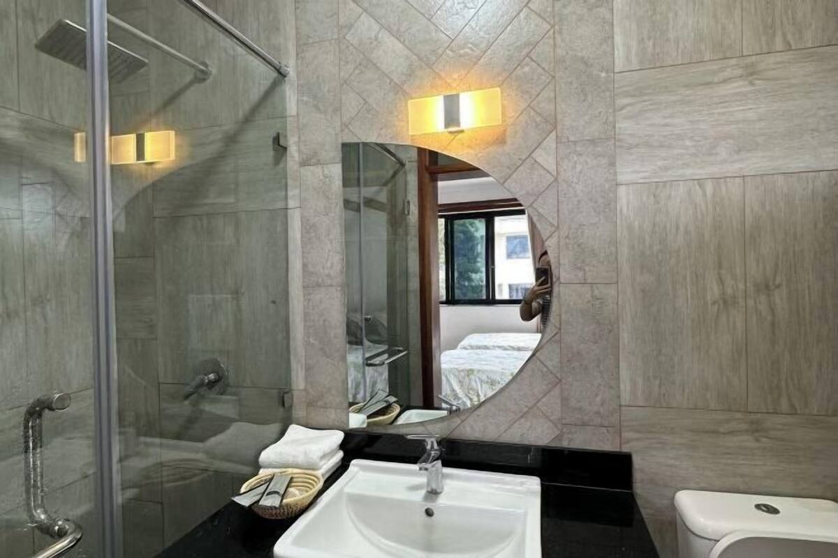 Un baño moderno con cabina de ducha de vidrio, un lavabo blanco y un espejo grande con espejo de aumento circular.