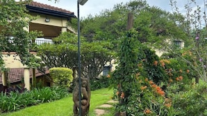 Un jardin avec un sentier, une sculpture et un bâtiment doté d’un toit en tuiles.