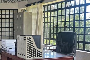 Ein Zimmer mit Schreibtisch, Stuhl, einem Fenster mit Blick auf Grünflächen und einer Kommode mit Schubladen.