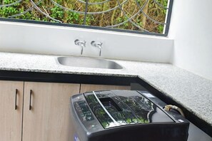 Een keuken met een inbouwtoaster, een raam met uitzicht op groen en een spoelbak met twee kraan.