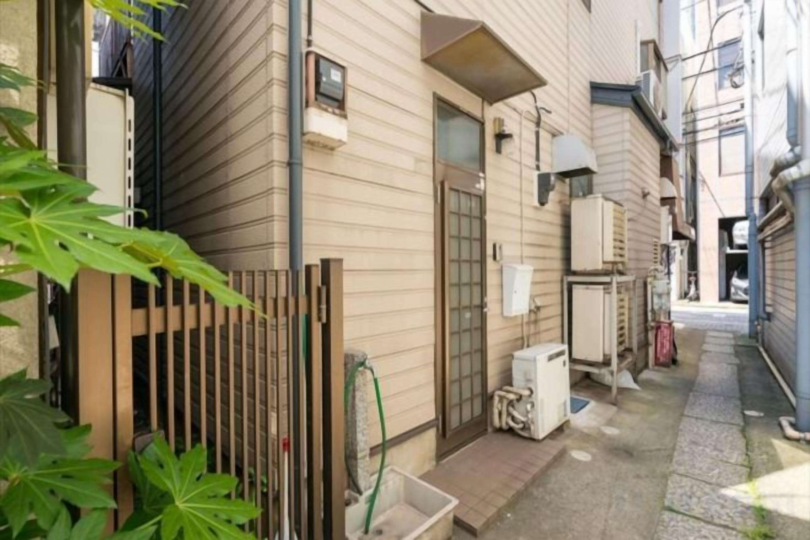 A narrow alleyway with a wooden fence, a small concrete planter, and a utility meter on the wall.