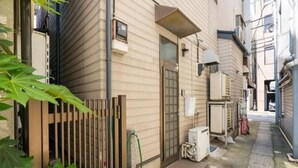 A narrow alleyway with a building on one side, a metal gate, and a small trash bin. - Tokyo Dome City Amusement Park Homestay (Tokyo)