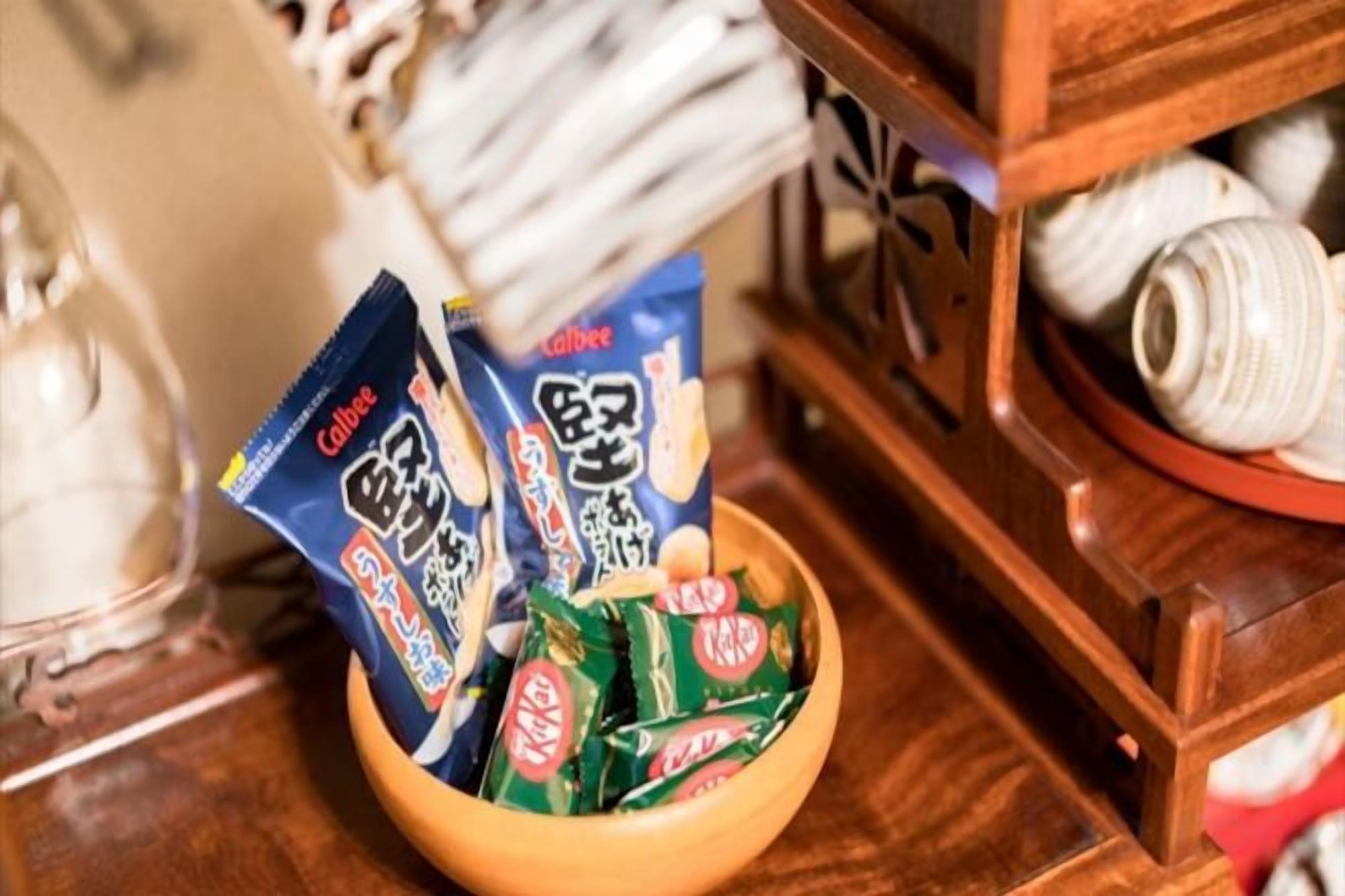 A wooden bowl containing packaged snacks and a ceramic plate with a white object.