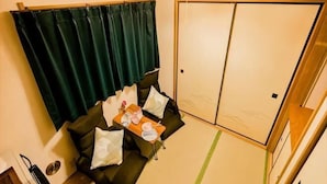 A room with a sofa, a small table with items, a sliding door, and a green curtain. - Tokyo Dome City Amusement Park Homestay (Tokyo)