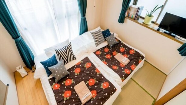 A bedroom with two beds, a TV, and a window with curtains. - Tokyo Dome City Amusement Park Homestay (Tokyo)