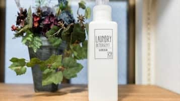 A bottle of laundry detergent on a wooden surface with a potted plant in the background.
