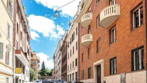 A narrow street lined with multi-story buildings, featuring balconies and a clear blue sky.