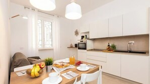 A modern kitchen with white cabinets, a dining table set with breakfast items, and a window with curtains.