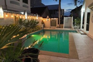 A swimming pool with a tiled edge, surrounded by potted plants and a stone wall. - royal park 217 (Pattaya)