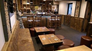 A cozy bar area with wooden furniture, a bar counter, and shelves stocked with bottles. - Greyhound Inn Freehouse  (Winterborne Kingston)