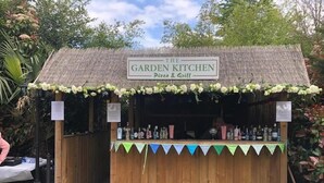 A wooden structure labeled "The Garden Kitchen Pizza & Grill" with a thatched roof and a variety of bottles on the counter. - Greyhound Inn Freehouse  (Winterborne Kingston)