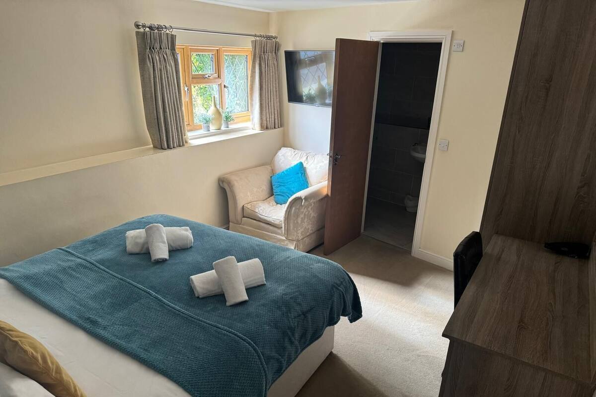 A bedroom with a bed, a chair, a wardrobe, and a bathroom door.