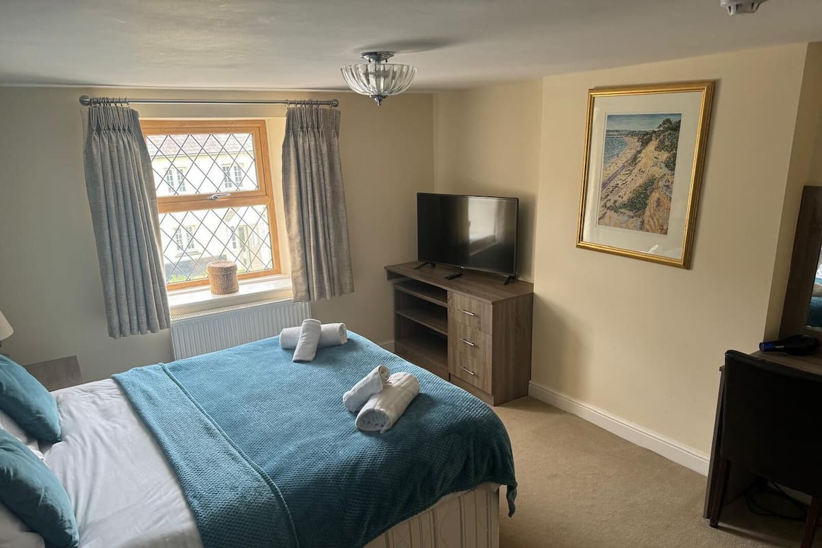 A bedroom with a bed, a TV, a painting, and a window with curtains.