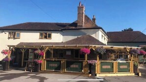 A traditional pub with a wooden exterior, a covered outdoor seating area, and hanging flower baskets. - Greyhound Inn Freehouse  (Winterborne Kingston)