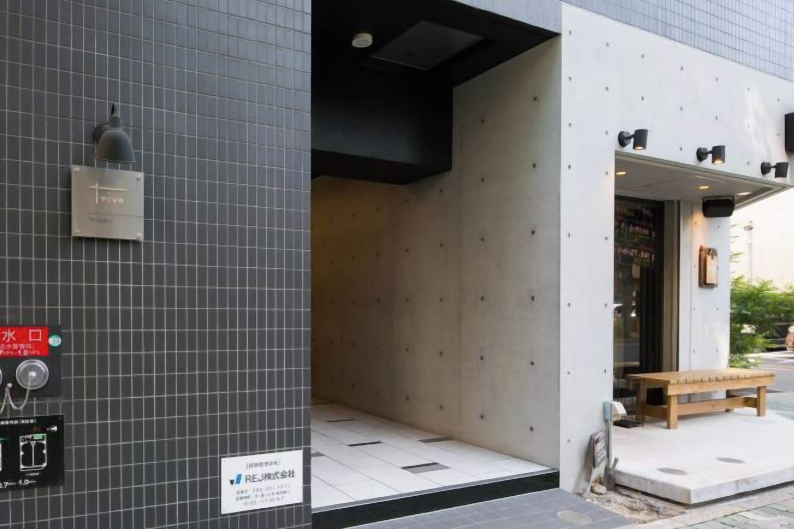 A building entrance with a tiled wall, a bench outside, and a sign with Japanese characters.