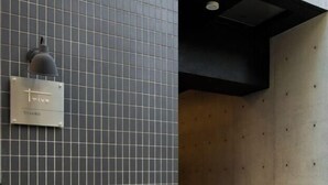 Eine mit Fliesen verkleidete Wand mit einer Tafel, auf der 'Triva' steht, und eine schwarze Decke mit einer eingelassenen Leuchte.