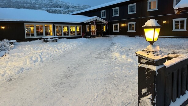 A hotel with a snow-covered landscape, a well-lit entrance, and a visible outdoor seating area. - Bjorliheimen Fjellhotell-Hotellrom (Lesja)