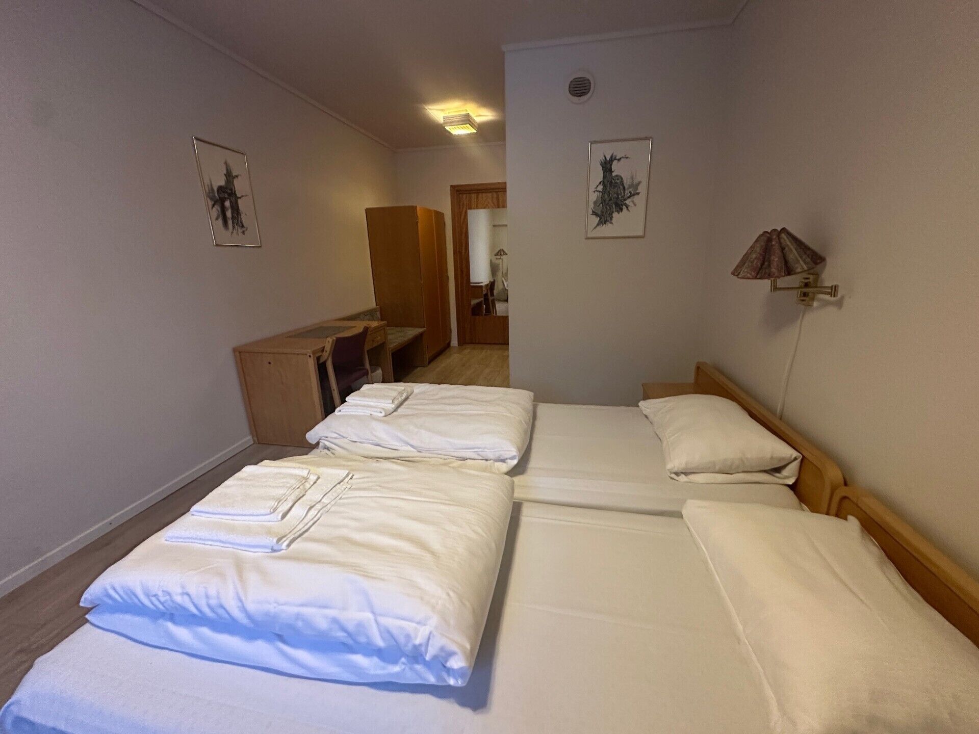 A hotel room with two beds, a desk, and a chair. There are two framed pictures on the walls.