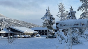 A snow-covered building with a sign indicating 'Bjorheimen' and a parking area with cars. - Bjorliheimen Fjellhotell-Hotellrom (Lesja)