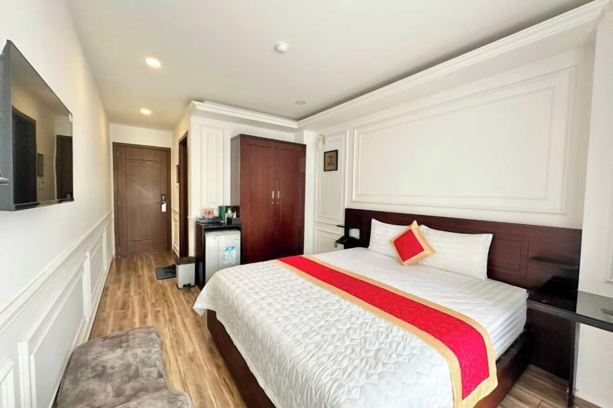 A hotel room with a large bed, a television, a desk, and a wardrobe.